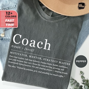 Puede incluir: Una camiseta gris oscuro con la palabra "Coach" en letras blancas grandes. La definición de entrenador está impresa debajo. La camiseta también tiene un gráfico que dice "12+ Colores" y "Tiempo de procesamiento rápido".