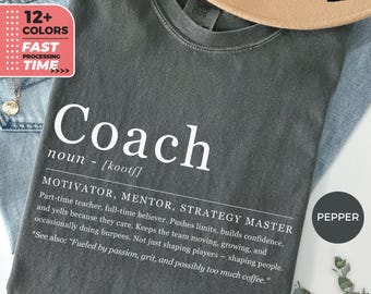 May include: A dark grey t-shirt with the word "Coach" in large white letters. The definition of coach is printed below. The shirt also has a graphic that says "12+ Colours" and "Fast Processing Time."