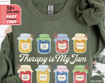 May include: Military green sweatshirt featuring the text "Therapy is My Jam" and jam jar illustrations with positive affirmations such as "Listen Deeply" and "Empathy." Available in 12+ colours.