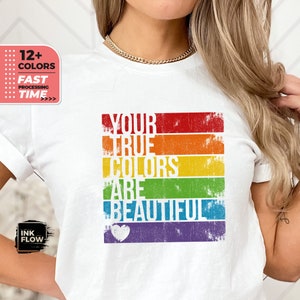 May include: White t-shirt featuring a rainbow design and the text "YOUR TRUE COLORS ARE BEAUTIFUL" in a vintage style font. A white heart is below the text.