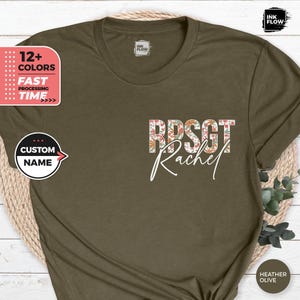 Può includere: Una t-shirt color oliva con un design floreale e il testo "RPSGT Rachel" stampato sul davanti.