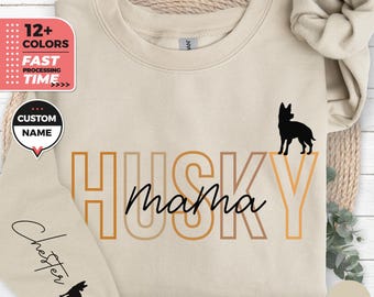 Op de afbeelding: Zandkleurige sweatshirt met de tekst "HUSKY mama" in een oranje en zwarte gradiënt, en een zwart silhouet van een hond. De mouw heeft de naam "Chester" en een honden silhouet. De afbeelding bevat ook de tekst "12+ KLEUREN" en "FAST PROCESSING TIME."