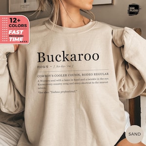 Könnte beinhalten: Ein sandfarbenes Sweatshirt mit dem Wort "Buckaroo" in Schwarz und einer Definition. Das Sweatshirt hat auch eine Grafik mit dem Text "12+ COLORS" und "FAST PROCESSING TIME".