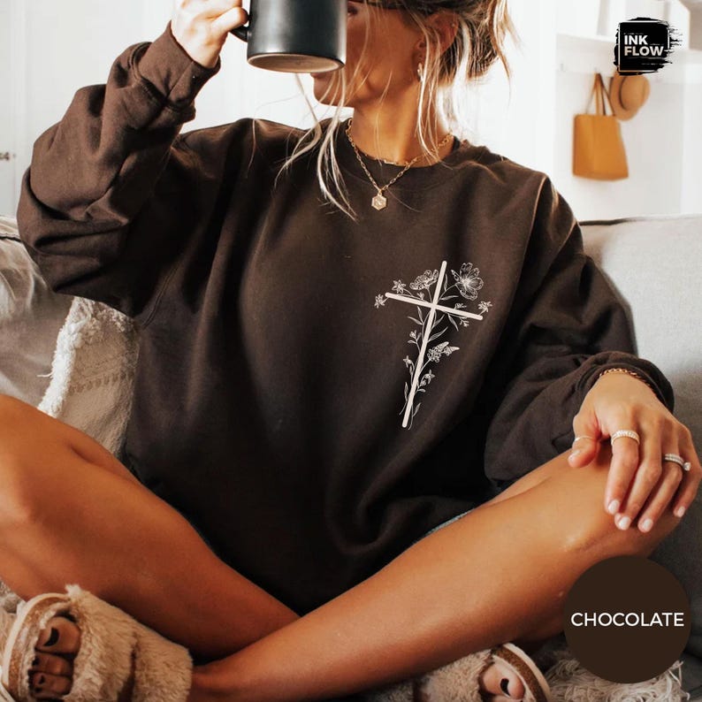 May include: Chocolate-coloured sweatshirt with a white floral cross design. The long-sleeved top is made of a soft material. A casual, comfortable garment. The word "chocolate" is visible in the image.