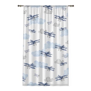 May include: White curtain with a repeating pattern of blue biplanes and fluffy blue and gray clouds. The biplanes are detailed with blue wings and silver bodies. The curtain is hung on a dark brown rod.