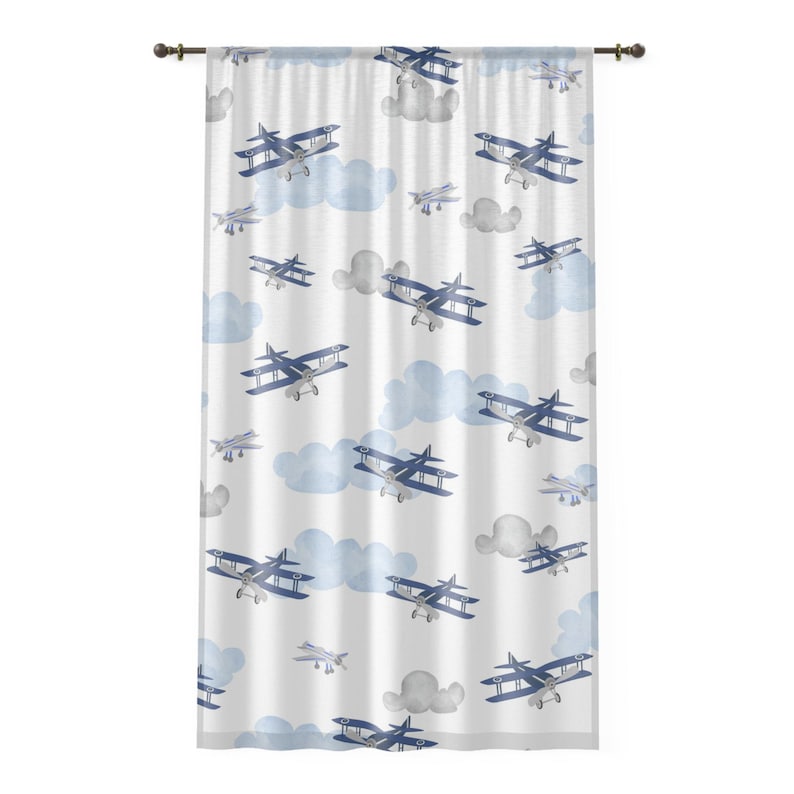 May include: White curtain with a repeating pattern of blue biplanes and fluffy blue and gray clouds. The biplanes are detailed with blue wings and silver bodies. The curtain is hung on a dark brown rod.