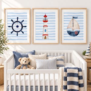 May include: Three framed wall art prints featuring nautical themes on a light blue and white striped background. The left print shows a dark blue ship wheel, the centre print depicts a red and white lighthouse, and the right print shows a sailboat.