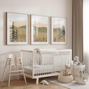 Könnte beinhalten: Ein weißes Babybett mit einem weißen und grauen Bettwäsche-Set. Über dem Babybett hängen drei gerahmte Drucke einer Aquarelllandschaft mit Bäumen und Bergen. Links vom Babybett steht ein weißer Hochstuhl. Auf dem Boden liegen Stofftiere und Körbe.