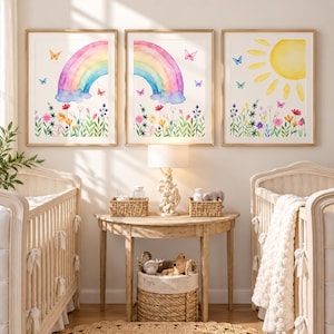 May include: Three framed wall art prints featuring watercolour illustrations. Two prints show a colourful rainbow over a field of wildflowers with butterflies, and one print displays a bright yellow sun above a similar floral meadow scene.