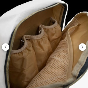 May include: A white canvas backpack with a black zipper and brown mesh lining. The backpack has multiple pockets and compartments.