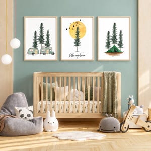 May include: Three framed wall art prints featuring watercolour illustrations of camping scenes. The left print shows a camper and trailer with pine trees. The centre print displays a yellow sun, a pine tree, and the text Little explorer. The right print shows a green tent.