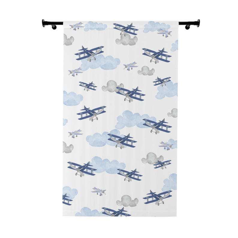 May include: White fabric shower curtain featuring a repeating pattern of blue biplanes and light blue clouds. The design includes gray clouds and smaller, single-wing planes. The curtain is hung on a black rod.
