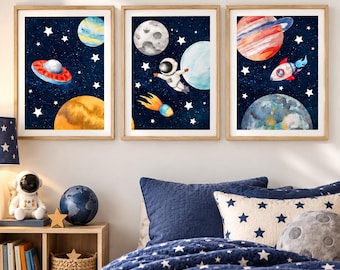 Pode incluir: Três quadros decorativos com ilustrações em aguarela de temática espacial. O primeiro mostra um OVNI e planetas, o segundo um astronauta e um cometa, e o terceiro um foguetão e planetas sobre um fundo azul escuro estrelado.