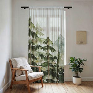 May include: A sheer window curtain featuring a watercolor-style print of evergreen trees and mountain peaks in shades of forest green, olive, and muted gray. The curtain hangs from a black rod, displaying a semi-transparent fabric texture.