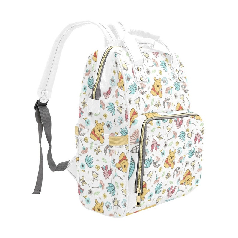 May include: White diaper bag backpack with a Winnie the Pooh print. The print features Winnie the Pooh, butterflies, and flowers in shades of pink, blue, yellow, and green.