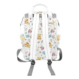 May include: White canvas backpack with a Winnie the Pooh and Piglet print. The backpack has adjustable straps and a top handle.