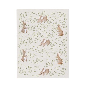 May include: A cream-colored blanket featuring a repeating pattern of watercolor-style brown bunnies and green leafy vines. The bunnies are in various poses, creating a whimsical and nature-inspired design.