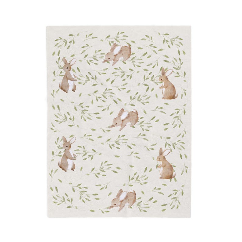 May include: A cream-colored blanket featuring a repeating pattern of watercolor-style brown bunnies and green leafy vines. The bunnies are in various poses, creating a whimsical and nature-inspired design.