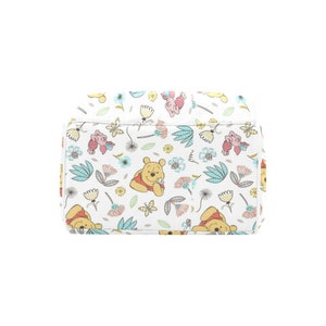 May include: A white canvas tote bag with a repeating pattern of Winnie the Pooh and Piglet characters, flowers, and leaves. The characters are in shades of yellow, pink, and red, and the flowers are in shades of pink, blue, and yellow.