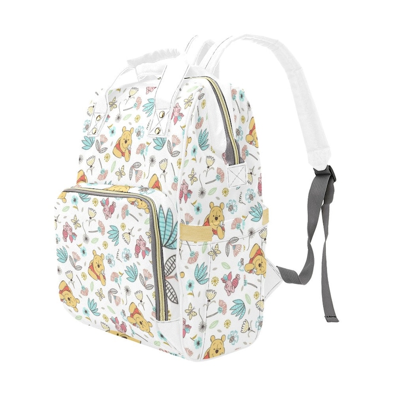 May include: White diaper bag backpack with a Winnie the Pooh floral print. The bag has multiple pockets and a zipper closure.
