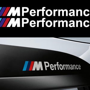 以下が含まれることがあります： 黒の背景に、青、赤、白のストライプが入った白い「M Performance」ロゴ。ロゴは2回繰り返されています。ロゴは、黒と白の車のバンパーにも表示されています。