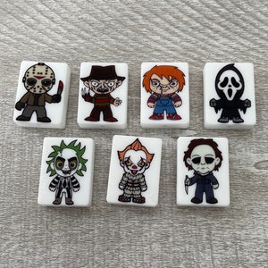May include: Set of seven white ceramic tiles with colorful illustrations of horror movie characters. The characters include Jason Voorhees, Freddy Krueger, Chucky, Ghostface, The Joker, Pennywise, and Michael Myers.