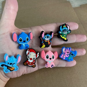 May include: A set of eight blue, pink, and green Stitch character shoe charms. The charms feature Stitch in various poses, including playing guitar, wearing a Santa hat, and holding a broom.