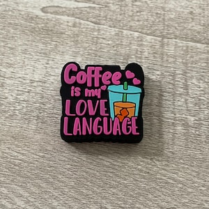 May include: Pink and black charm with the text "Coffee is my love language" and a cartoon image of a blue and orange iced coffee cup with a straw.