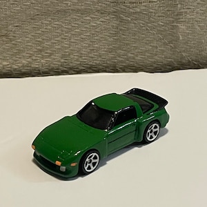 May include: A green toy car with black accents and black wheels. The car has a spoiler on the back.