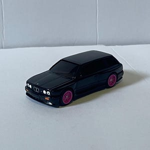 May include: Black toy car with pink wheels. The car is a wagon style and has a detailed front end.