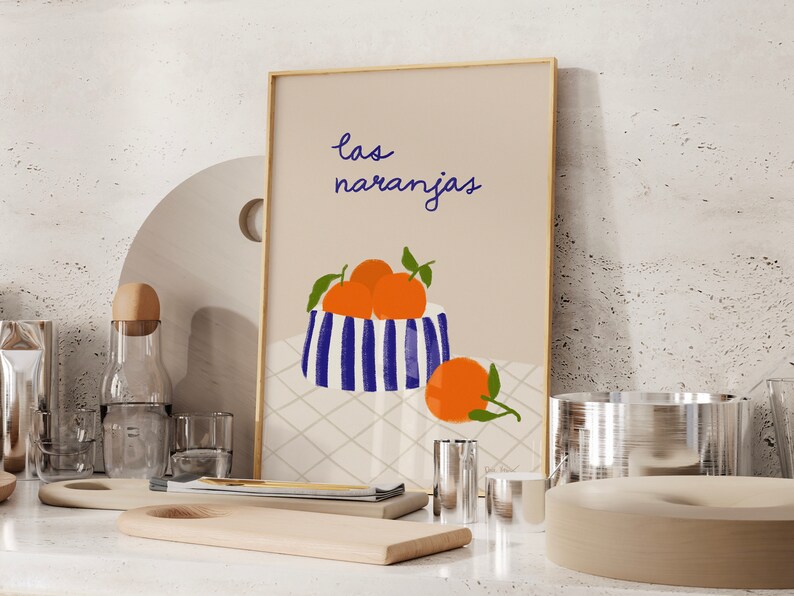 May include: A beige framed print with the text "las naranjas" in blue cursive. The print features a blue and white striped bowl filled with orange oranges and a single orange on the table below the bowl.