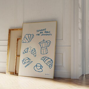 Op de afbeelding: Een wit canvas met blauwe inkttekeningen van croissants, een koffiepot en een kopje koffie. De tekst "Sundays are made for croissants" is in blauwe inkt op het canvas geschreven.