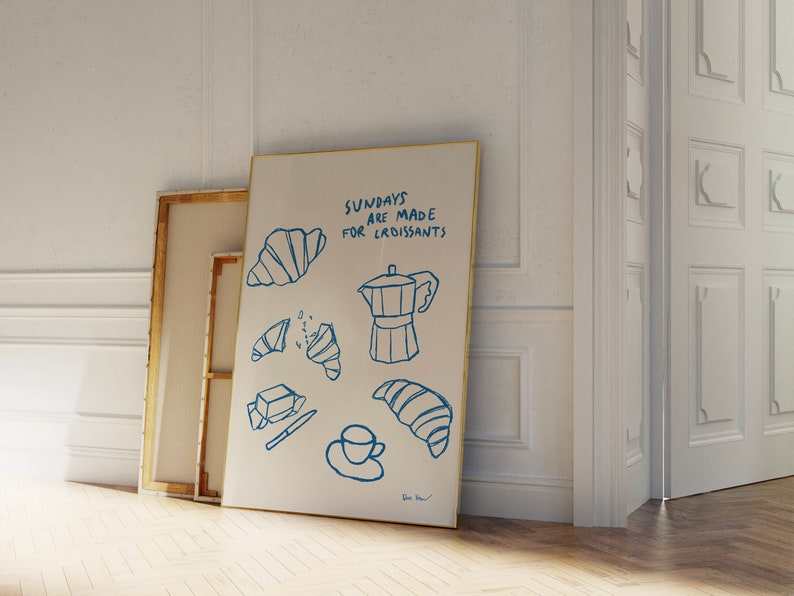 Op de afbeelding: Een wit canvas met blauwe inkttekeningen van croissants, een koffiepot en een kopje koffie. De tekst "Sundays are made for croissants" is in blauwe inkt op het canvas geschreven.