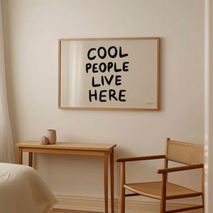 Può includere: Una stampa incorniciata con il testo "COOL PEOPLE LIVE HERE" in font calligrafico nero su sfondo bianco.