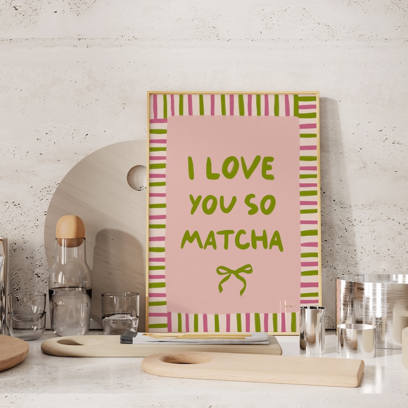 May include: A pink and green striped framed print with the text "I love you so matcha" in green lettering. A green bow is below the text.