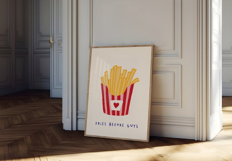 May include: A framed art print featuring a whimsical illustration of a container of golden french fries. The container is red and white striped with a heart. The text "FRIES BEFORE GUYS" is written below the fries.