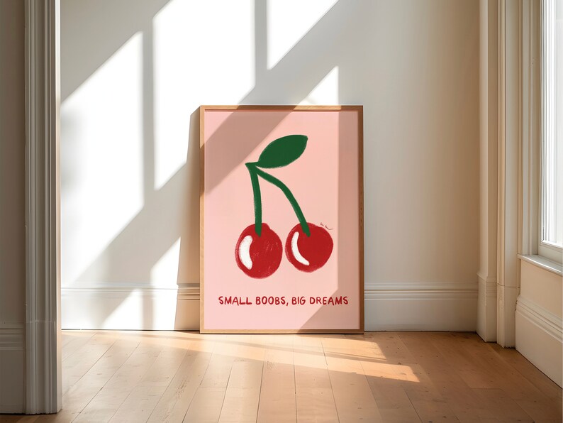 K&ouml;nnte beinhalten: Ein rosa gerahmtes Poster mit einer Zeichnung von zwei roten Kirschen mit gr&uuml;nen Stielen und Bl&auml;ttern. Der Text "SMALL BOOBS, BIG DREAMS" ist unter den Kirschen gedruckt.