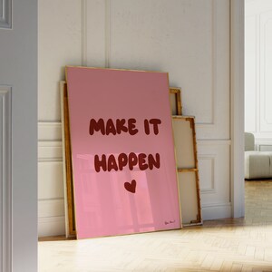 Könnte beinhalten: Ein rosa gerahmter Leinwanddruck mit dem Text "MAKE IT HAPPEN" in roten Buchstaben und einem kleinen roten Herzen. Der Druck lehnt an einer weißen Wand.