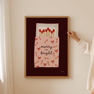 May include: A pink and red matchbox with the text "merry and bright" printed on it. The matchbox is filled with red matches and is set against a dark red background.