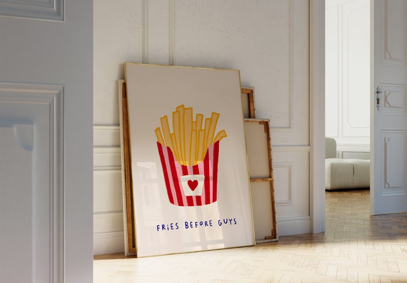 May include: A framed art print featuring a cartoon illustration of a container of french fries. The fries are golden yellow, and the container is red and white striped with a heart. The text "FRIES BEFORE GUYS" is written in blue.