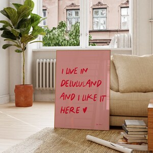 以下が含まれることがあります： 赤い文字で「I live in Delululand and I like it here &hearts;」と書かれたピンクのポスターです。