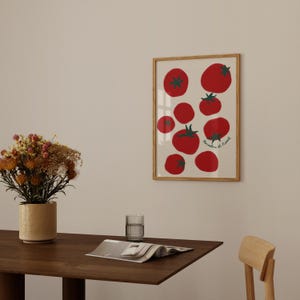 May include: A framed art print featuring a collection of red tomatoes with green stems and leaves on a cream background. The print has a wooden frame and the text "Pomodorini di Napoli" in green. The artwork is displayed on a wall.