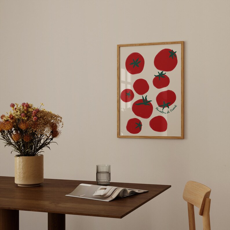 May include: A framed art print featuring a collection of red tomatoes with green stems and leaves on a cream background. The print has a wooden frame and the text "Pomodorini di Napoli" in green. The artwork is displayed on a wall.