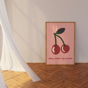 K&ouml;nnte beinhalten: Ein rosa Poster mit einer Grafik von zwei roten Kirschen und dem Text "SMALL BOOBS, BIG DREAMS".