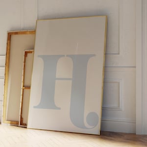 May include: Two framed canvases leaning against a white wall. The larger canvas features a light blue letter "H" in a stylised font. The smaller canvas is wooden and has a white surface.