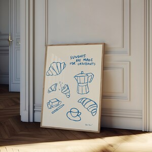 Op de afbeelding: Een witte poster met blauwe tekst en illustraties van croissants, boter, een mes, een kopje koffie en een koffiepot. De tekst luidt "Zondagen zijn gemaakt voor croissants".