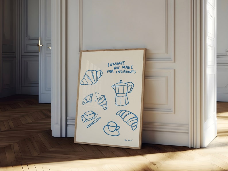 Op de afbeelding: Een witte poster met blauwe tekst en illustraties van croissants, boter, een mes, een kopje koffie en een koffiepot. De tekst luidt "Zondagen zijn gemaakt voor croissants".