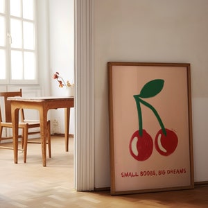 K&ouml;nnte beinhalten: Ein gerahmter Druck mit rosa Hintergrund, auf dem ein gr&uuml;ner Stiel und zwei rote Kirschen abgebildet sind. Unter den Kirschen steht der Text "SMALL BOOBS, BIG DREAMS".