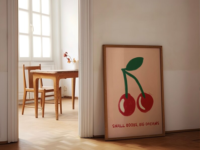 K&ouml;nnte beinhalten: Ein gerahmter Druck mit rosa Hintergrund, auf dem ein gr&uuml;ner Stiel und zwei rote Kirschen abgebildet sind. Unter den Kirschen steht der Text "SMALL BOOBS, BIG DREAMS".