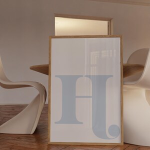 May include: A framed print featuring a light blue letter "H" on a white background. The frame is made of natural wood.